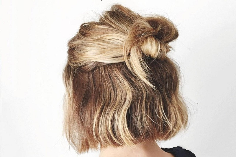 Cô gái với mái tóc ngắn búi củ tỏi xinh xắn, mặc áo dài trắng tinh khôi, thể hiện sự trẻ trung và đáng yêu