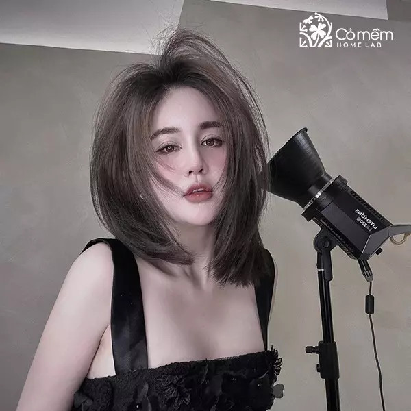 Cô gái với mái tóc ngắn uốn xoăn đuôi nhẹ, màu nâu sáng, tạo vẻ dịu dàng cho khuôn mặt vuông