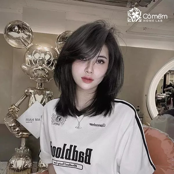 Cô gái với tóc ngắn layer ngang vai màu nâu sáng, tóc mái dài uốn nhẹ giúp làm mềm đường nét mặt vuông