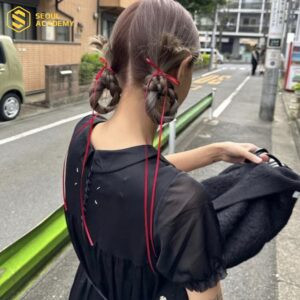 Kiểu tóc thắt bím cuộn vòng gọn gàng, tô điểm nơ nhỏ xinh xắn, rất dễ thương.