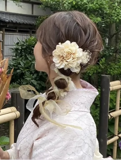 Một cô gái trẻ với kiểu tóc đuôi ngựa được uốn nhẹ, tô điểm bằng phụ kiện hoa tươi, mặc kimono màu xanh pastel dịu dàng, tạo nên phong cách trẻ trung và thanh lịch tại Asakusa.