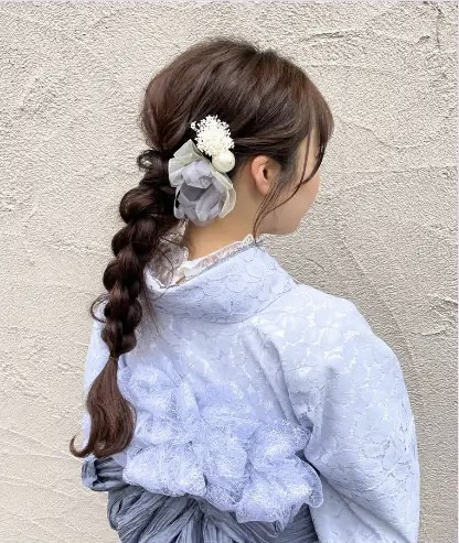 Một cô gái với kiểu tóc bện dài được nới lỏng nhẹ nhàng, kết hợp cùng hoa cài tóc tinh tế, tạo nên vẻ đẹp dịu dàng và nữ tính khi mặc kimono, minh họa một trong số kiểu tóc bện được ưa chuộng tại Lyve.
