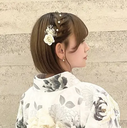 Một phụ nữ với kiểu tóc bob ngắn được tạo kiểu nhẹ nhàng và trang trí bằng kẹp tóc hình hoa, mặc kimono màu hồng pastel, thể hiện vẻ đẹp trẻ trung và thanh lịch, minh họa một số kiểu tóc bob phù hợp với kimono tại Lyve.