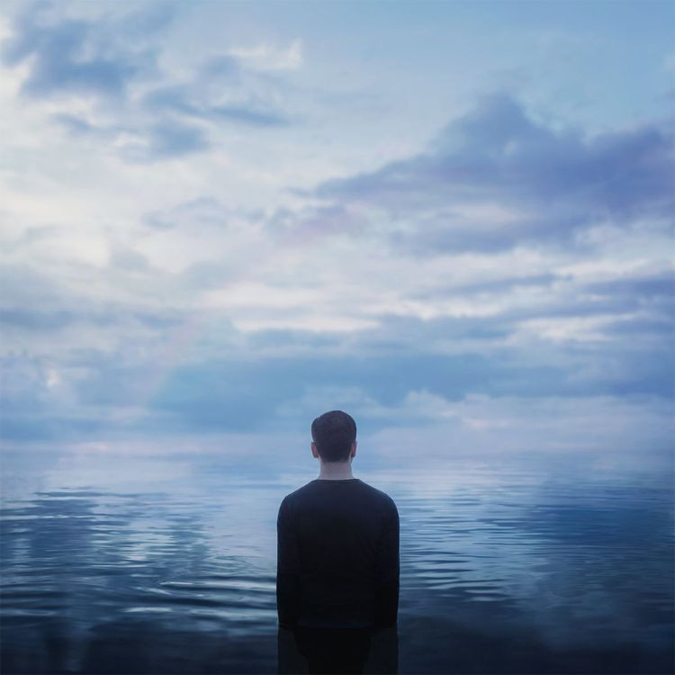 Người đàn ông ngồi một mình trên ghế đá công viên, cúi đầu suy tư, thể hiện sự mệt mỏi và nỗi buồn kín đáo từ phía sau