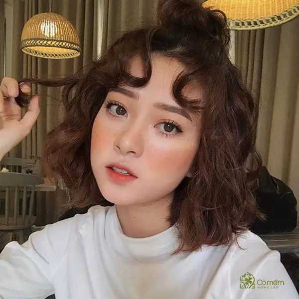 Tóc ngắn xoăn tít kiểu hippie, màu nâu, giúp làm đầy đặn và mềm mại các đường nét mặt vuông