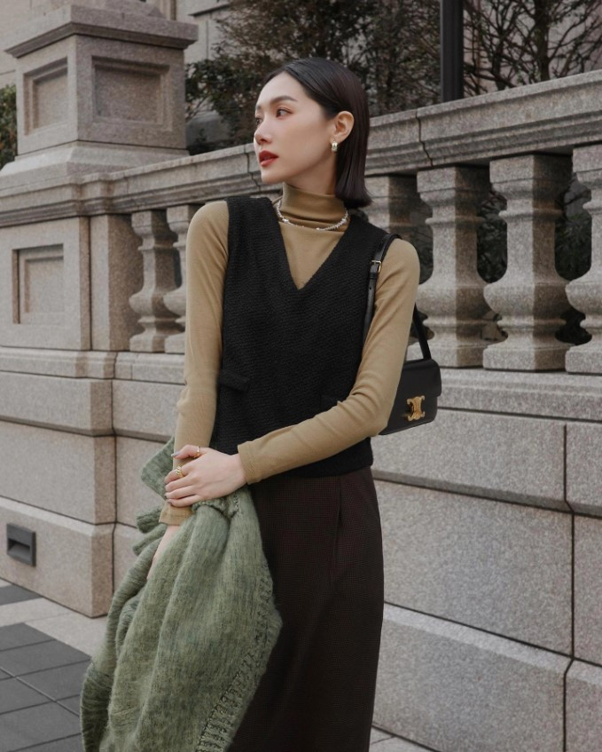 Cô gái tóc ngắn mặc áo gile len, áo sơ mi và chân váy dài, phong cách mùa đông ấm áp