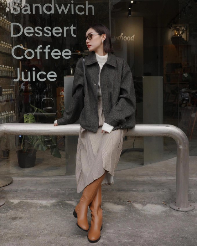 Cô gái tóc ngắn mặc áo khoác dạ, chân váy xếp ly và boot cao cổ, phong cách mùa đông