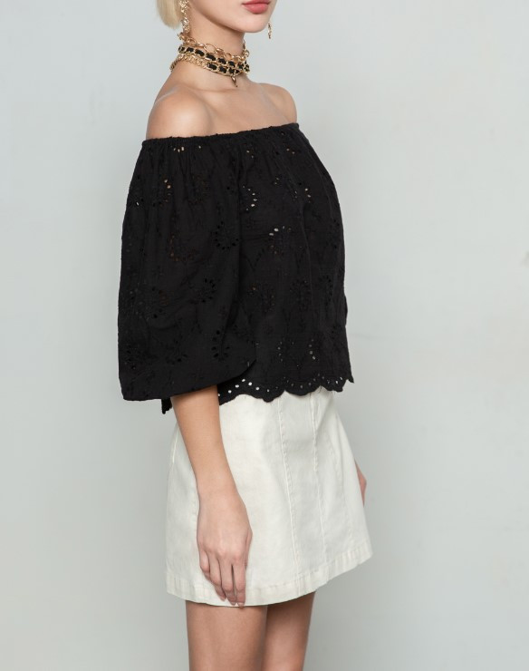 Cô gái tóc ngắn mặc áo trễ vai kẻ sọc và chân váy trắng, mang phong cách thanh lịch