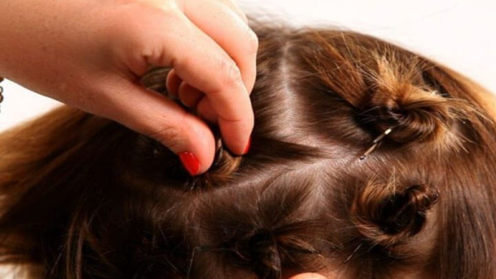 Cô gái trẻ đang tạo kiểu tóc xoăn tại nhà bằng cách dùng dây thun buộc các lọn tóc ngắn đã xoắn.